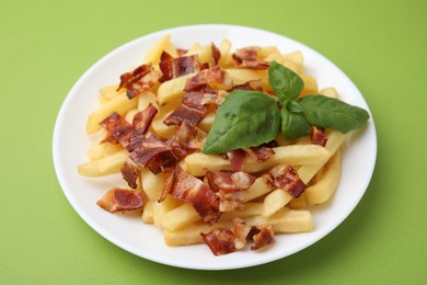 Photo of Delicious French fries with slices of bacon and basil on green background, closeup