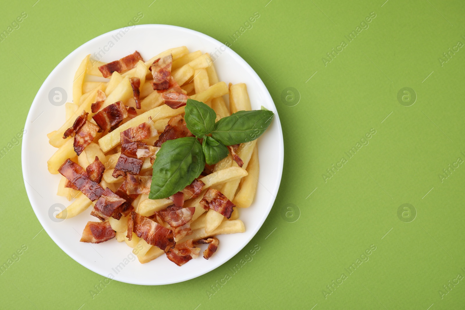 Photo of Delicious French fries with bacon and basil on green background, top view. Space for text