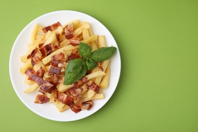 Delicious French fries with bacon and basil on green background, top view. Space for text