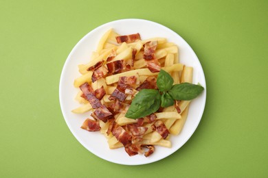 Photo of Delicious French fries with slices of bacon and basil on green background, top view