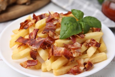 Delicious French fries with slices of bacon and basil on table, closeup