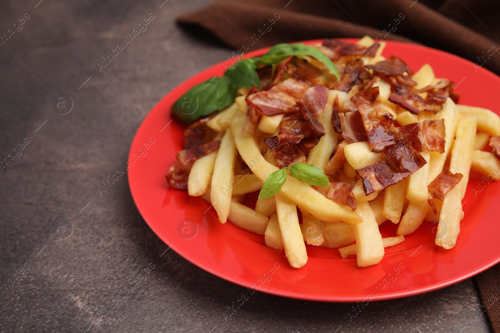 Photo of Delicious French fries with bacon and basil on brown background, closeup. Space for text