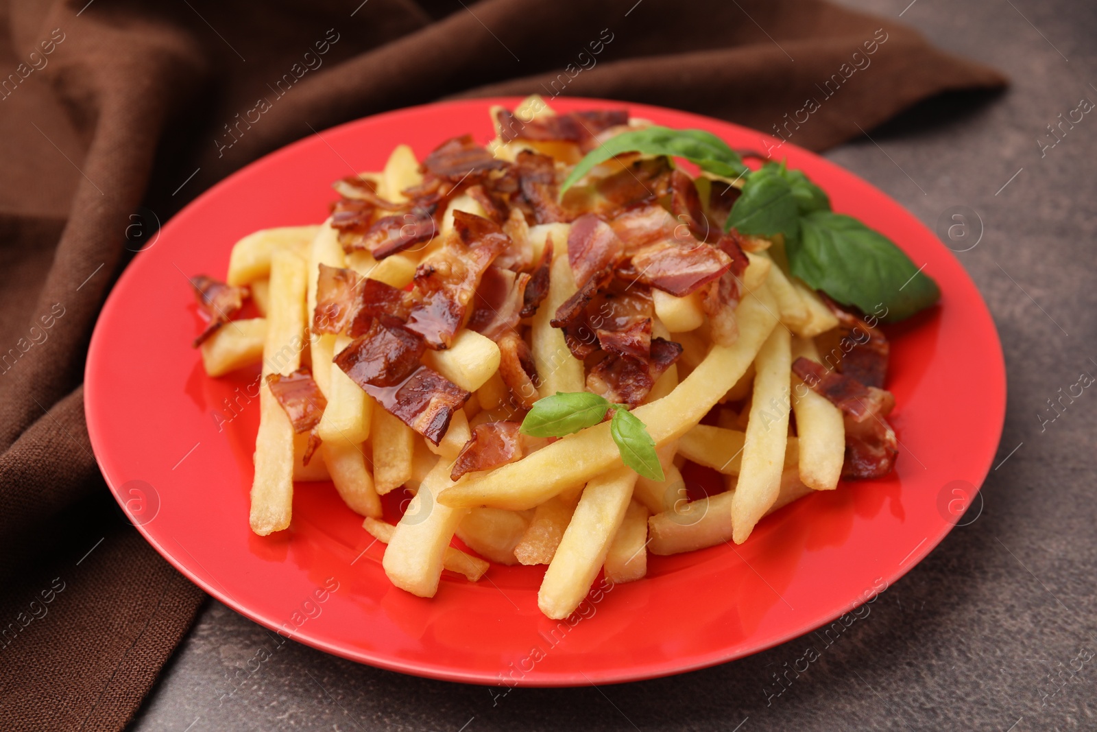 Photo of Delicious French fries with slices of bacon and basil on brown background, closeup