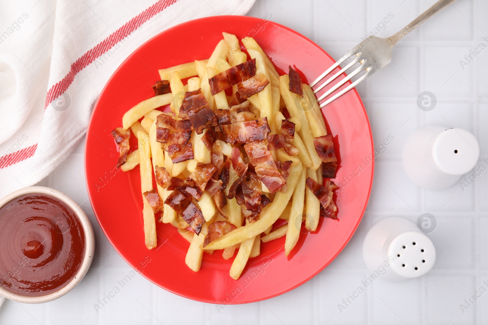 Photo of Delicious French fries with bacon served on white tiled table, flat lay