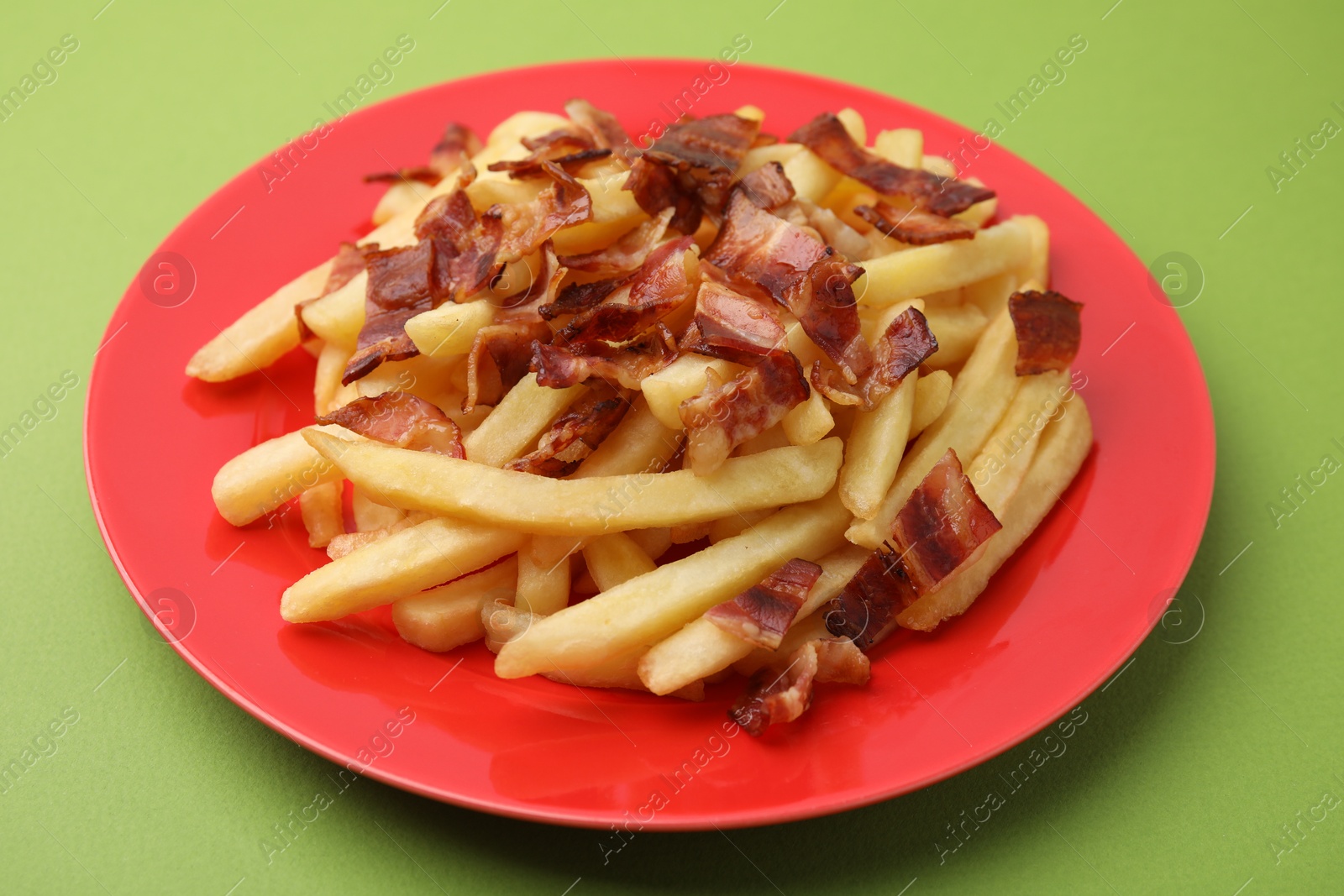 Photo of Delicious French fries with slices of bacon on green background, closeup