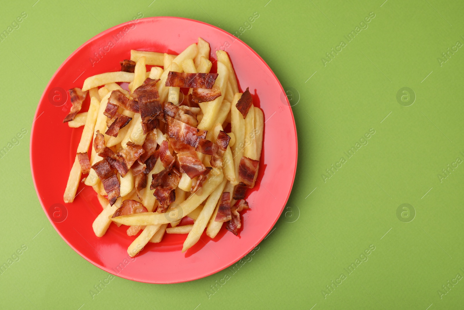 Photo of Delicious French fries with bacon on green background, top view. Space for text