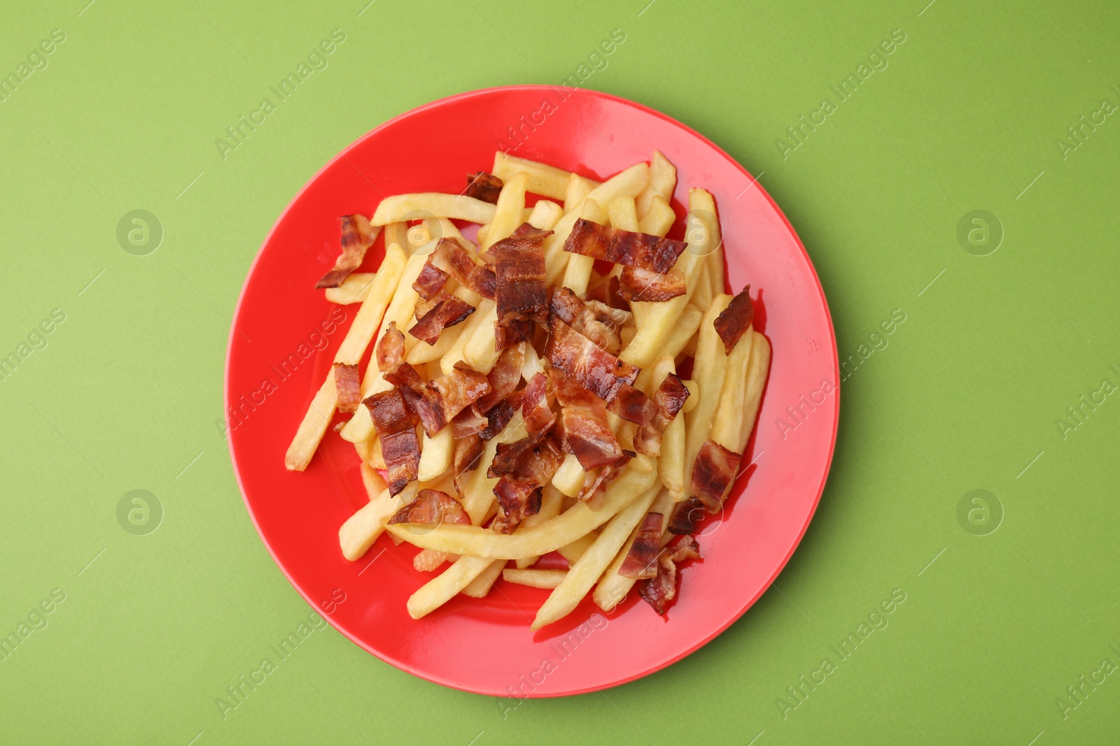 Photo of Delicious French fries with slices of bacon on green background, top view