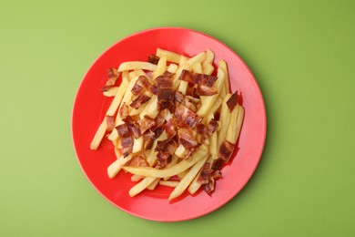 Photo of Delicious French fries with slices of bacon on green background, top view