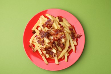 Delicious French fries with slices of bacon on green background, top view