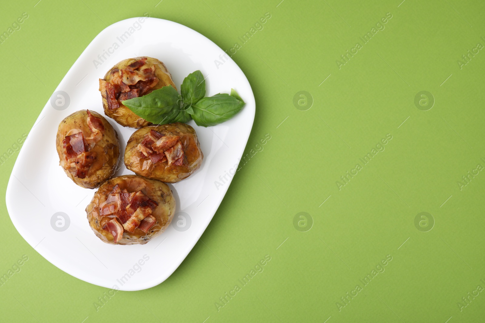 Photo of Delicious baked potatoes with bacon and basil on green background, top view. Space for text