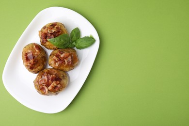 Photo of Delicious baked potatoes with bacon and basil on green background, top view. Space for text