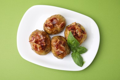 Delicious baked potatoes with bacon and basil on green background, top view