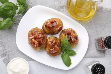 Delicious baked potatoes with bacon and basil on grey table, flat lay