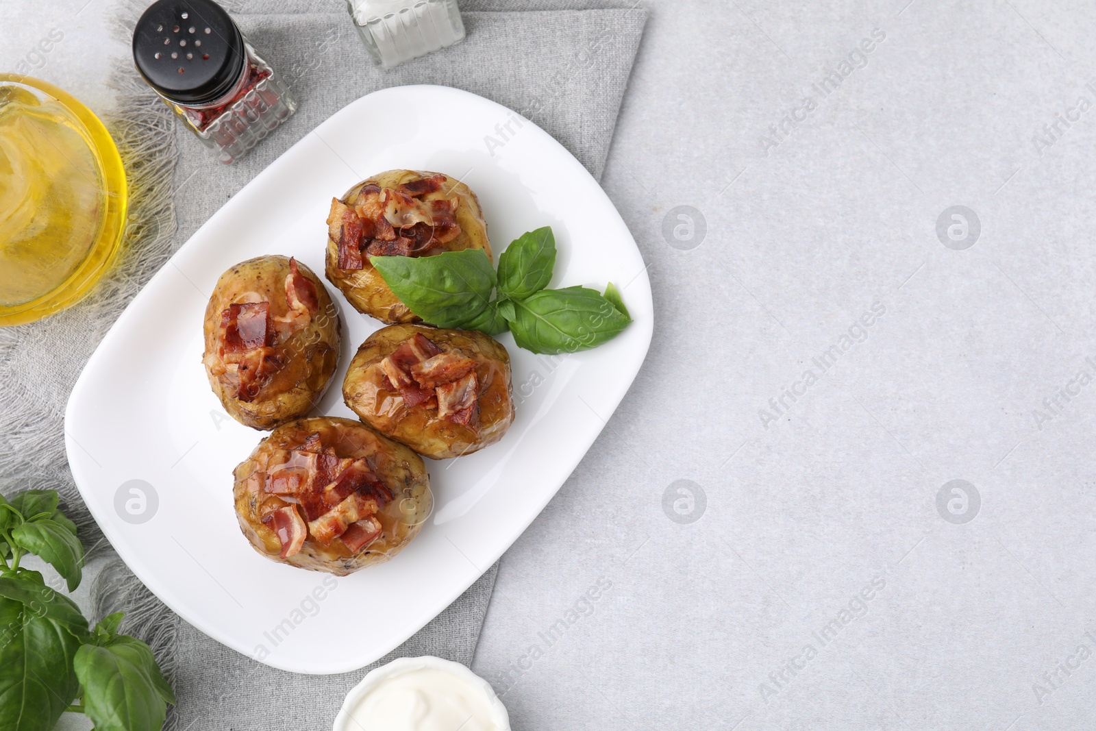 Photo of Delicious baked potatoes with bacon and basil on grey table, flat lay. Space for text