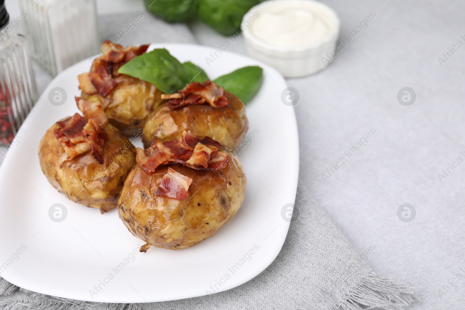 Photo of Delicious baked potatoes with bacon and basil on grey table, closeup. Space for text