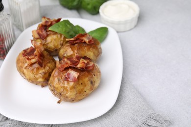 Delicious baked potatoes with bacon and basil on grey table, closeup. Space for text