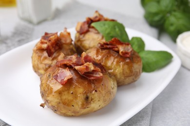 Delicious baked potatoes with bacon and basil on grey table, closeup