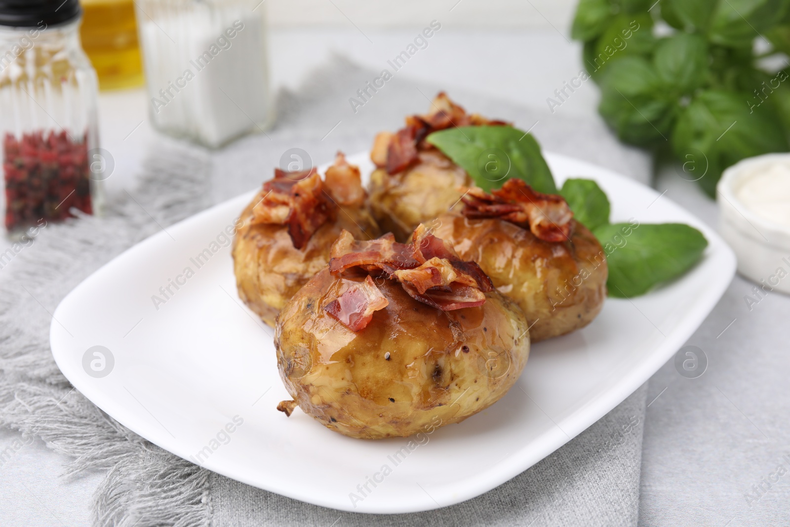 Photo of Delicious baked potatoes with bacon and basil on grey table, closeup