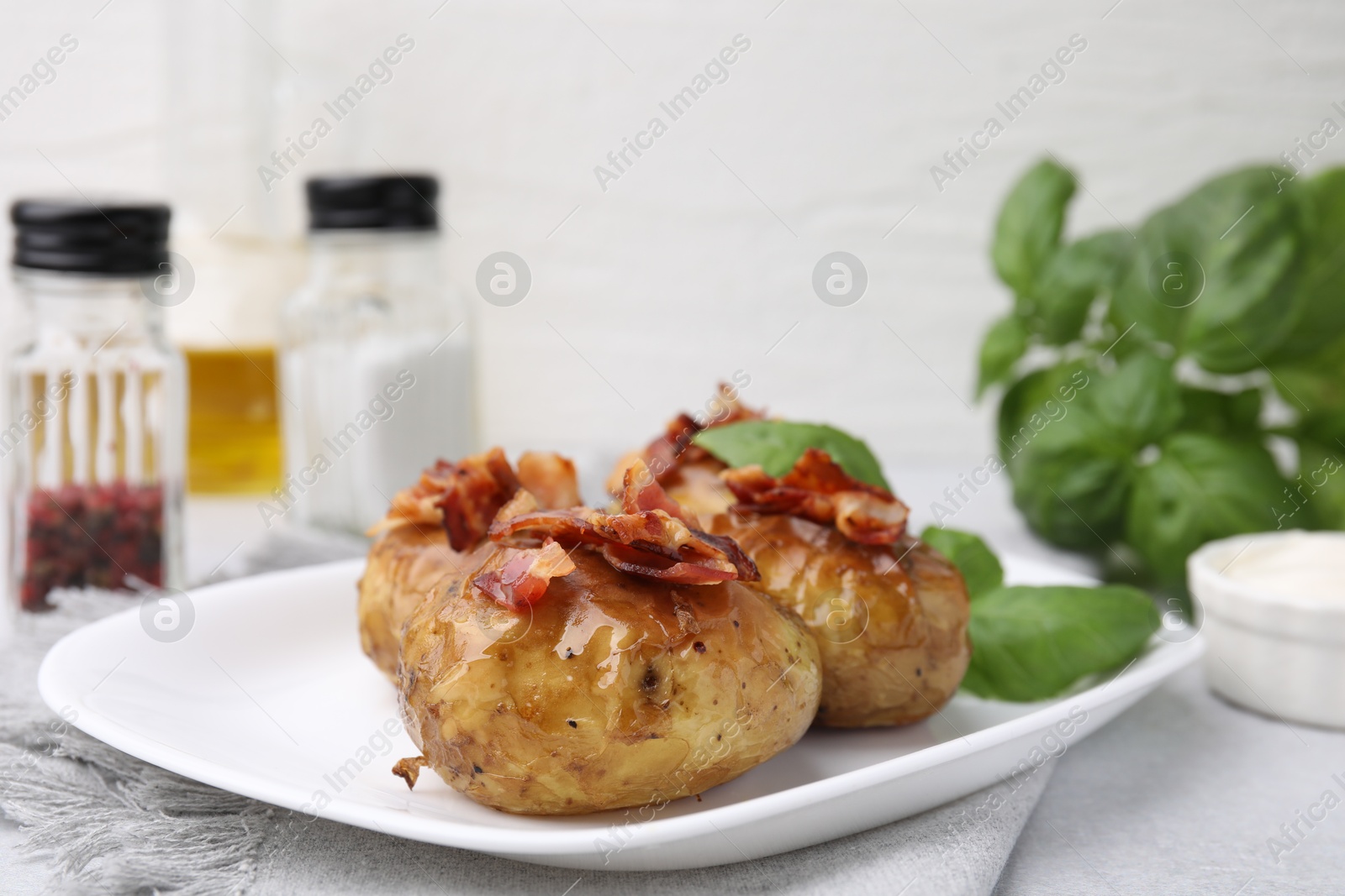 Photo of Delicious baked potatoes with bacon and basil on grey table, closeup