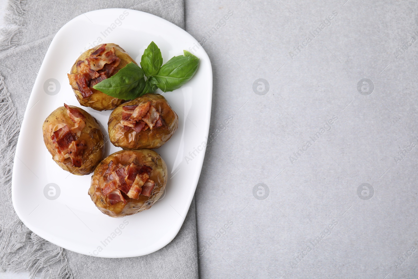 Photo of Delicious baked potatoes with bacon and basil on grey table, top view. Space for text