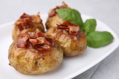 Delicious baked potatoes with bacon and basil on light table, closeup