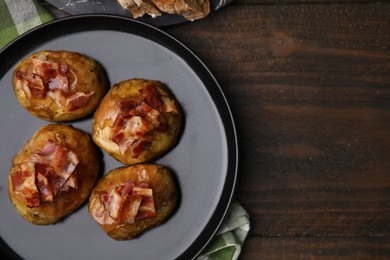 Photo of Delicious baked potatoes with bacon on wooden table, top view. Space for text