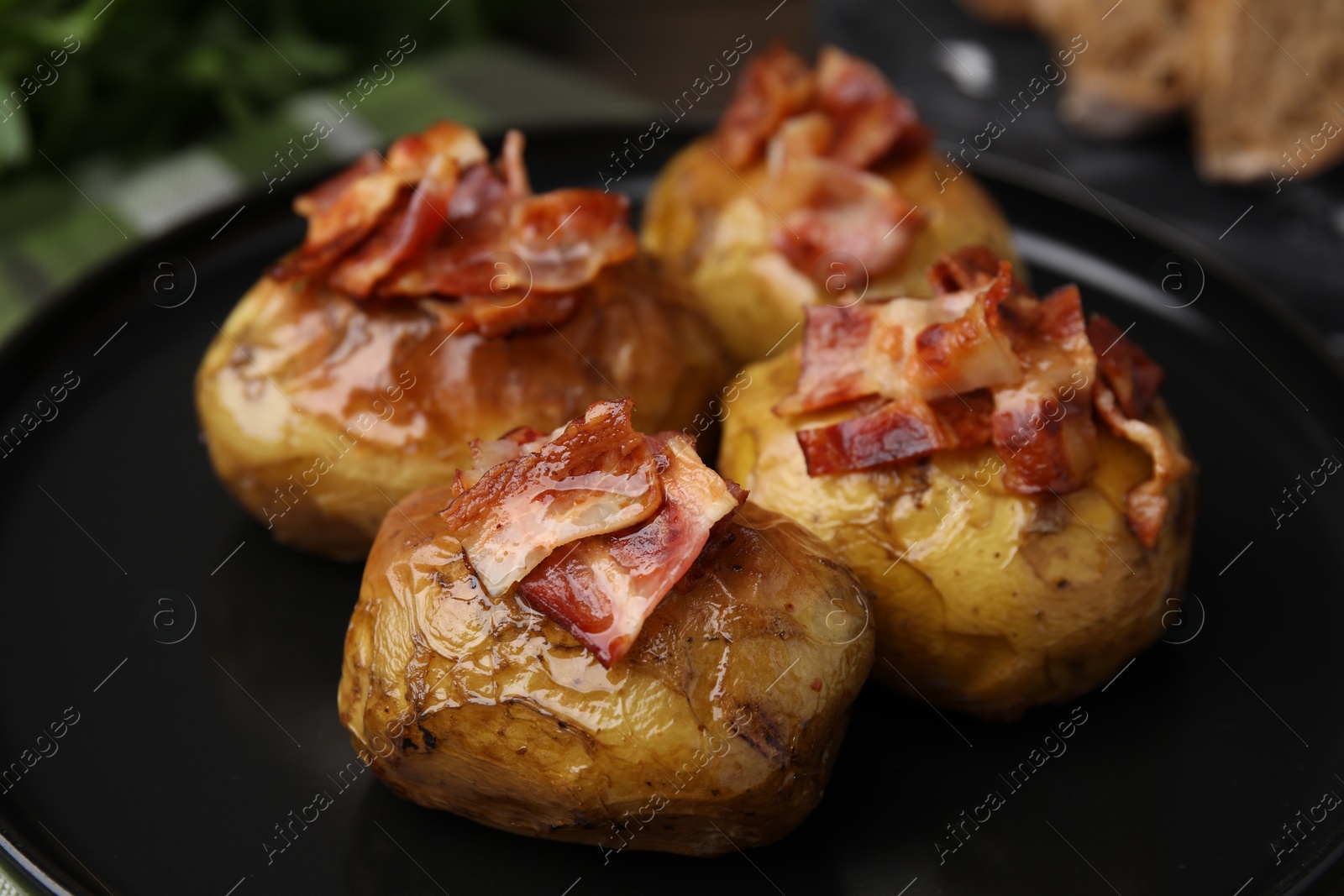 Photo of Delicious baked potatoes with bacon on black plate, closeup