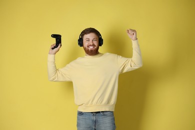 Happy man in headphones with game controller on pale yellow background