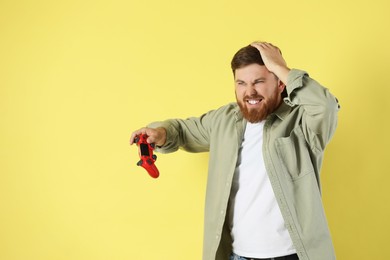 Confused man with game controller on pale yellow background. Space for text