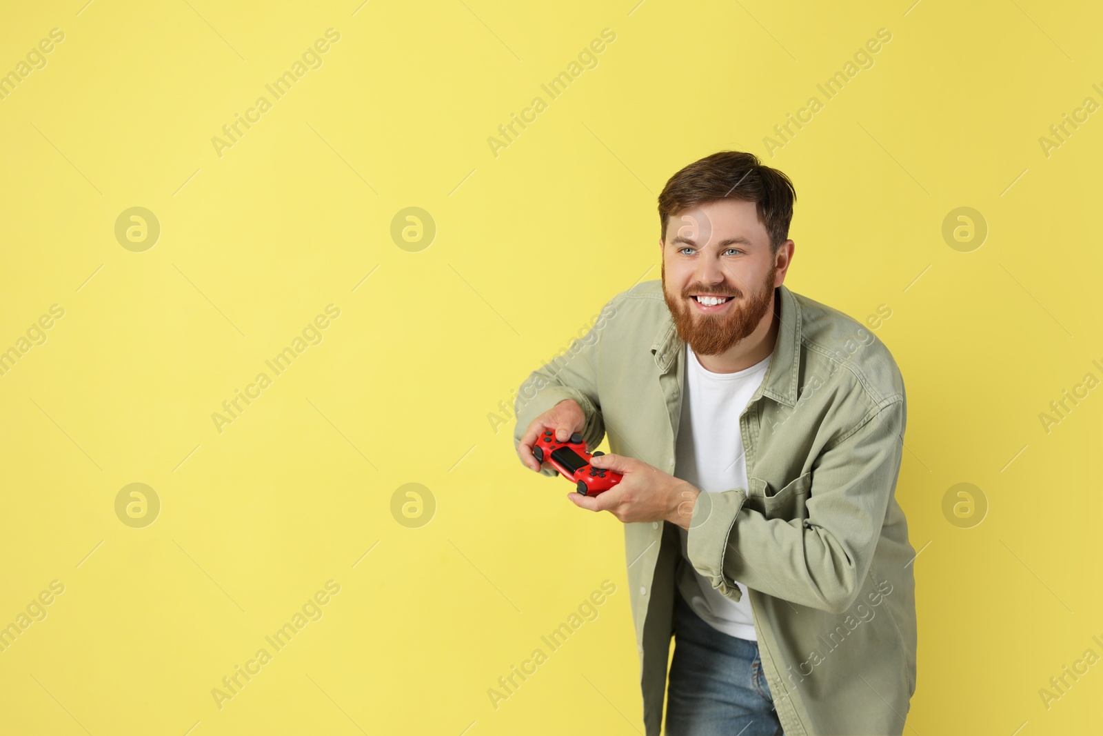 Photo of Happy man playing video game with controller on pale yellow background. Space for text