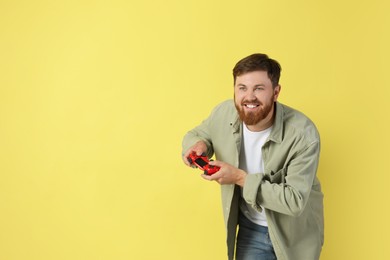 Photo of Happy man playing video game with controller on pale yellow background. Space for text