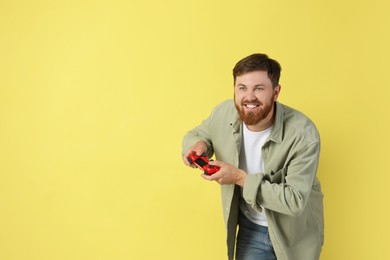 Happy man playing video game with controller on pale yellow background. Space for text