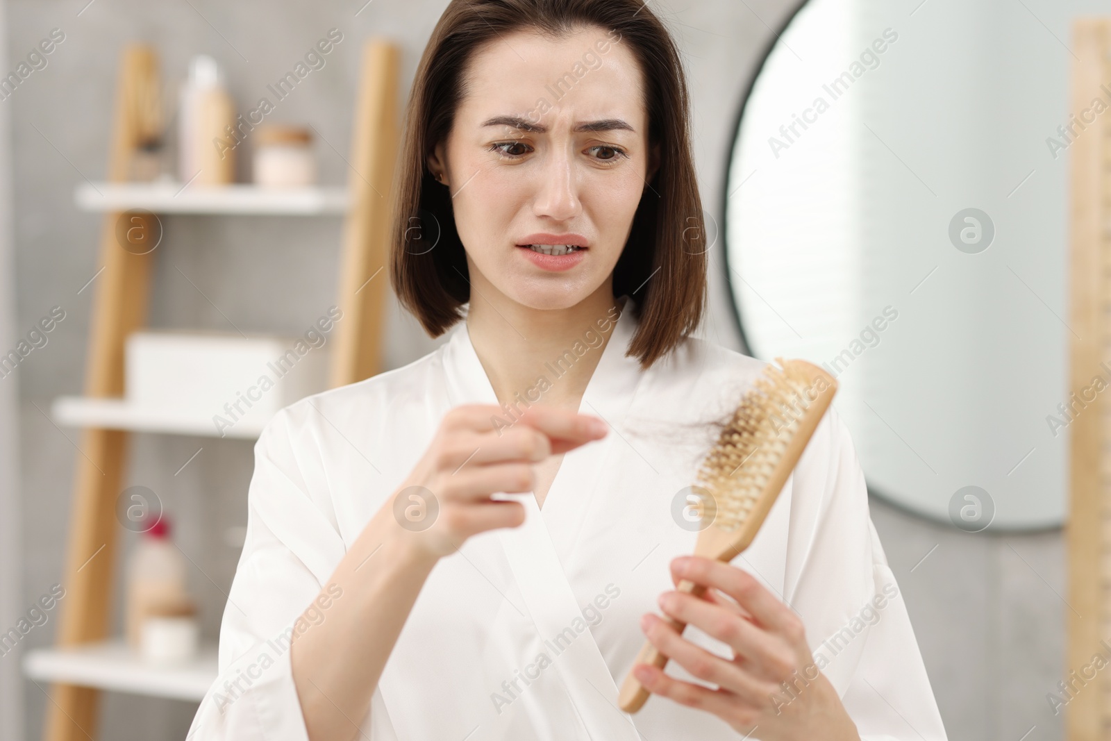 Photo of Stressed woman taking her lost hair from brush in bathroom. Alopecia problem