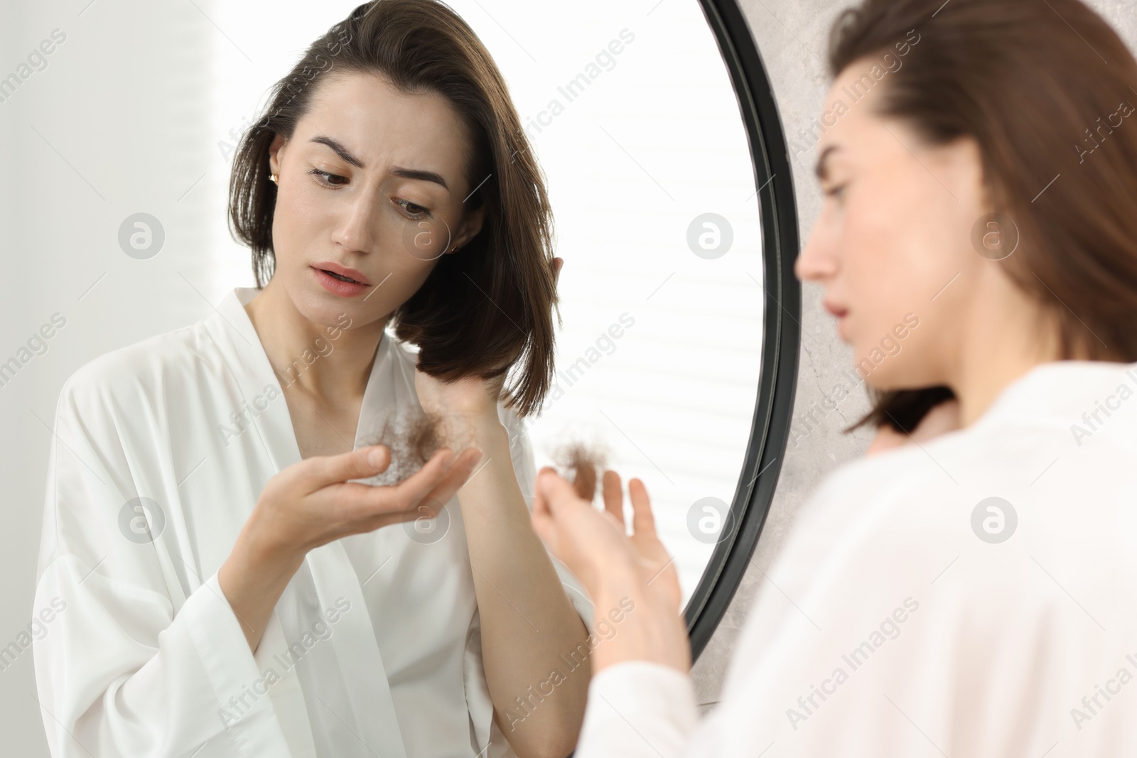 Photo of Sad woman holding clump of lost hair near mirror indoors. Alopecia problem