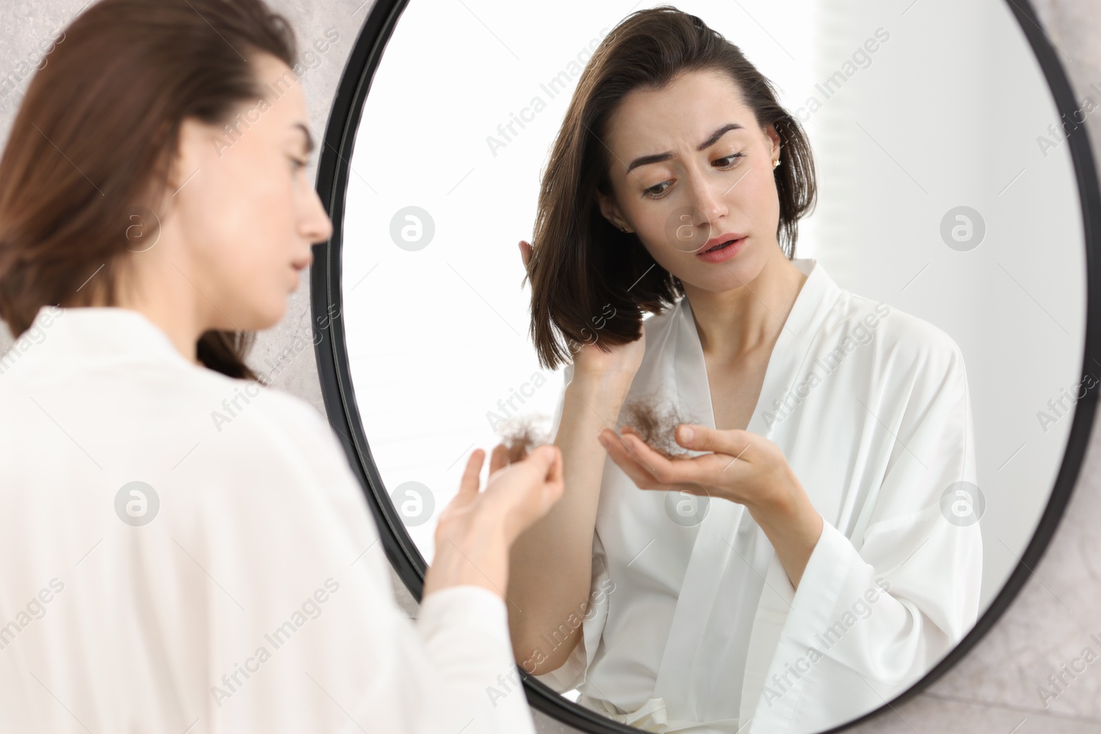 Photo of Sad woman holding clump of lost hair near mirror indoors. Alopecia problem