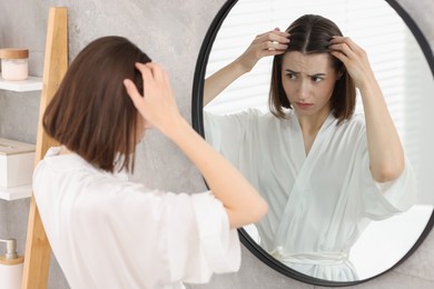 Photo of Young woman with hair loss problem looking at mirror indoors