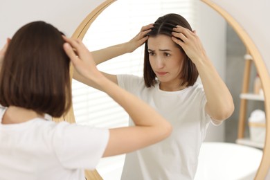 Sad woman with hair loss problem looking at mirror indoors