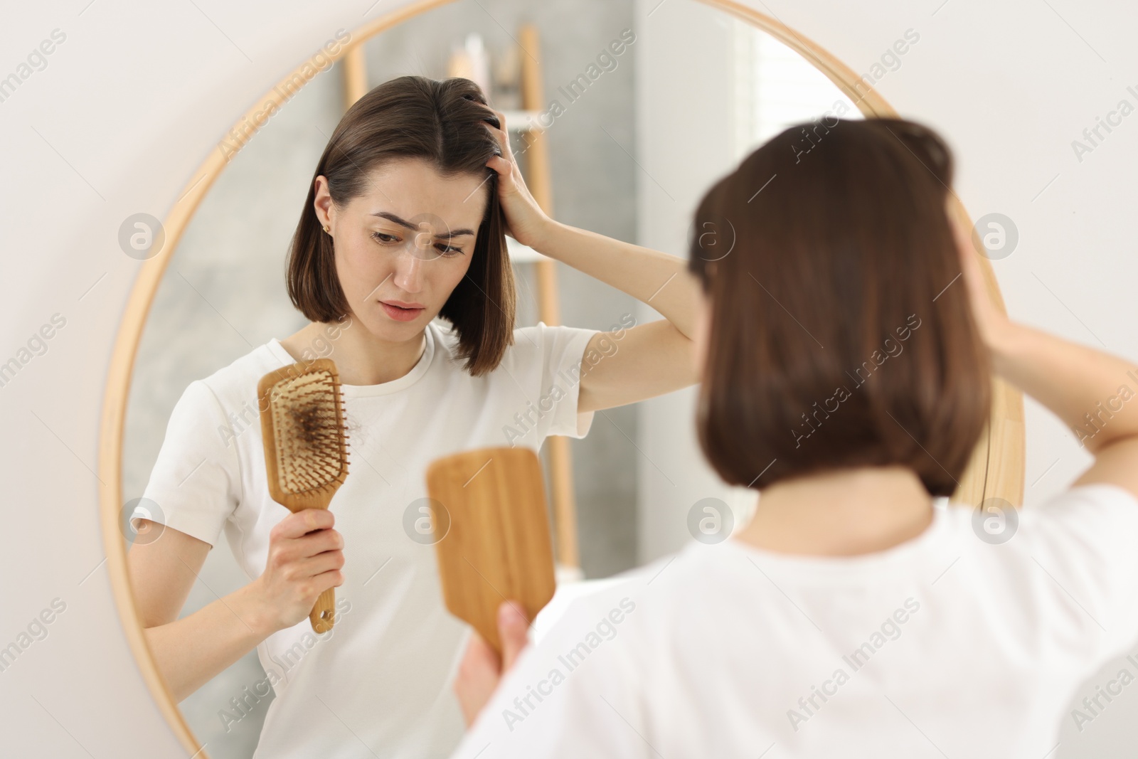 Photo of Sad woman holding brush with lost hair indoors. Alopecia problem