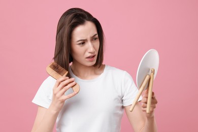 Sad woman with hair loss problem looking at mirror on pink background