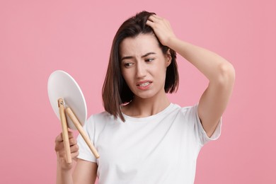 Photo of Sad woman with hair loss problem looking at mirror on pink background