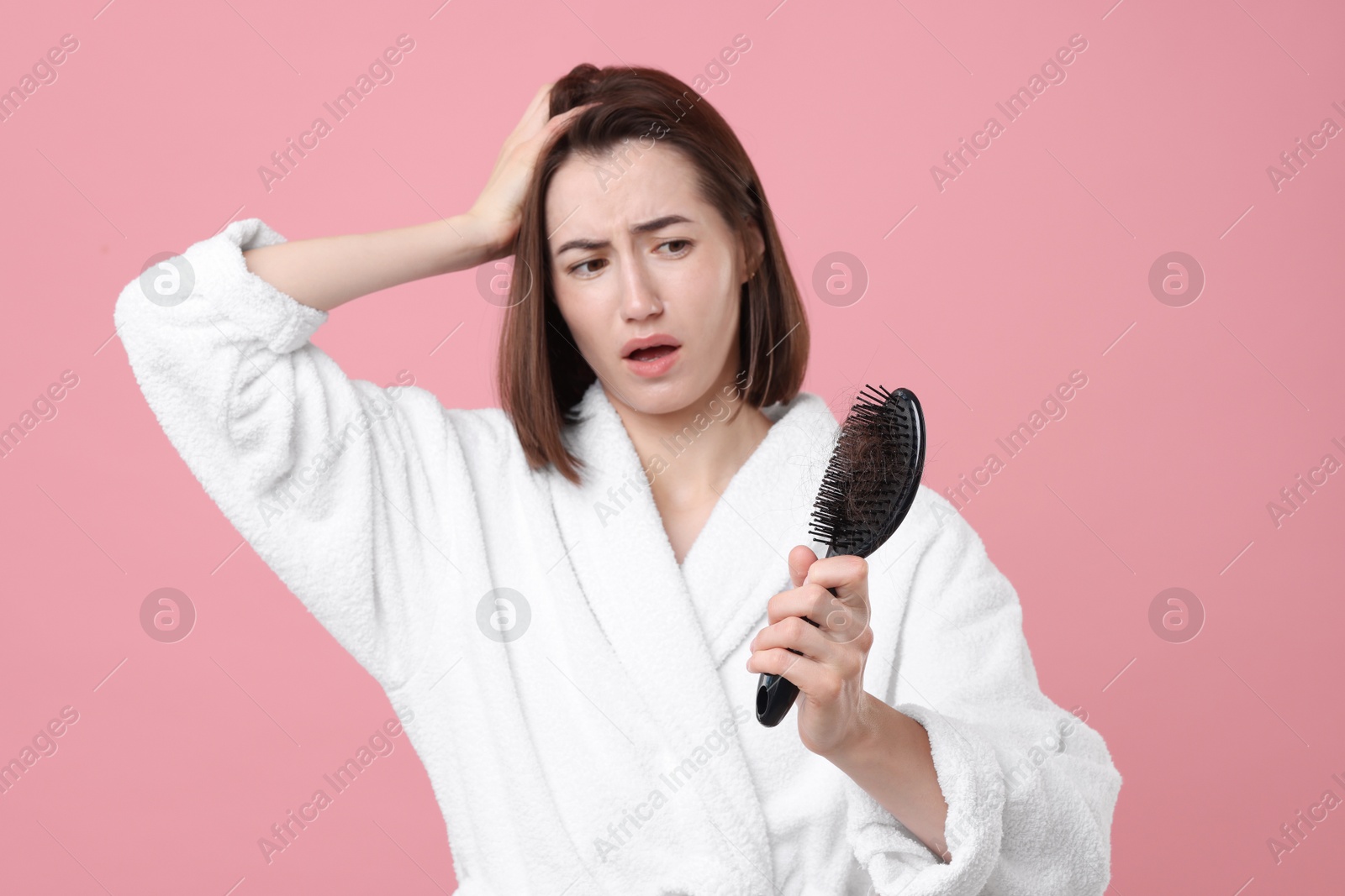 Photo of Emotional woman holding brush with lost hair on pink background. Alopecia problem