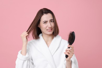 Photo of Emotional woman holding brush with lost hair on pink background. Alopecia problem