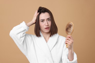 Stressed woman holding brush with lost hair on light brown background. Alopecia problem