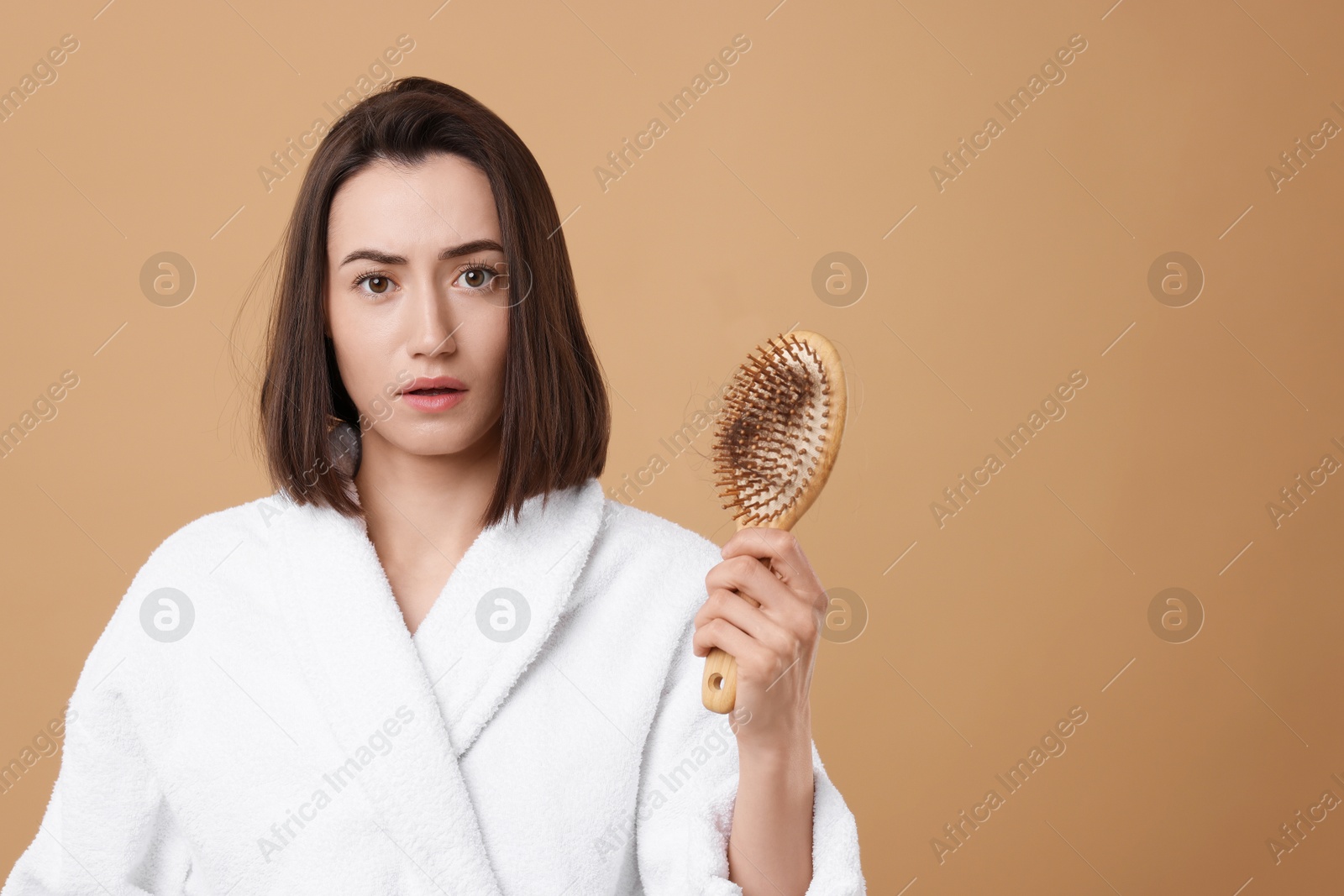 Photo of Sad woman holding brush with lost hair on light brown background, space for text. Alopecia problem