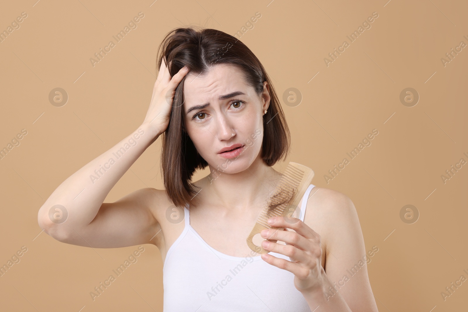 Photo of Stressed woman holding comb with lost hair on light brown background. Alopecia problem