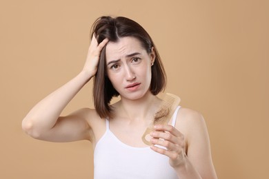 Stressed woman holding comb with lost hair on light brown background. Alopecia problem