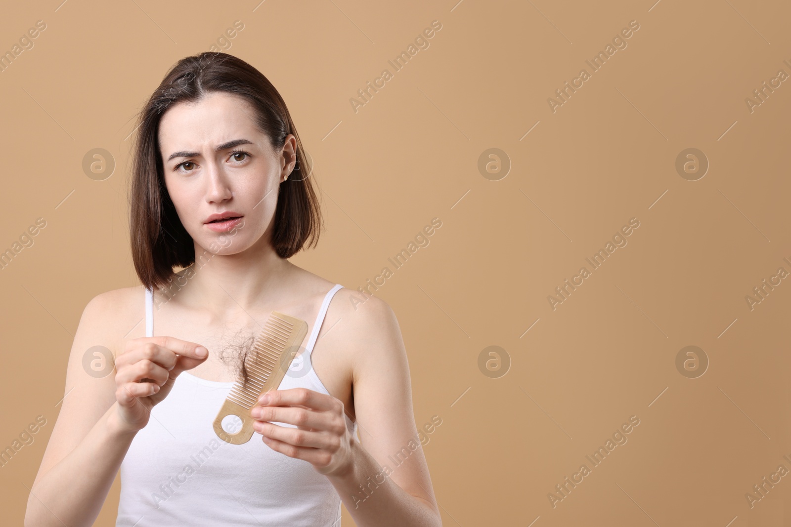 Photo of Sad woman taking her lost hair from comb on light brown background, space for text. Alopecia problem