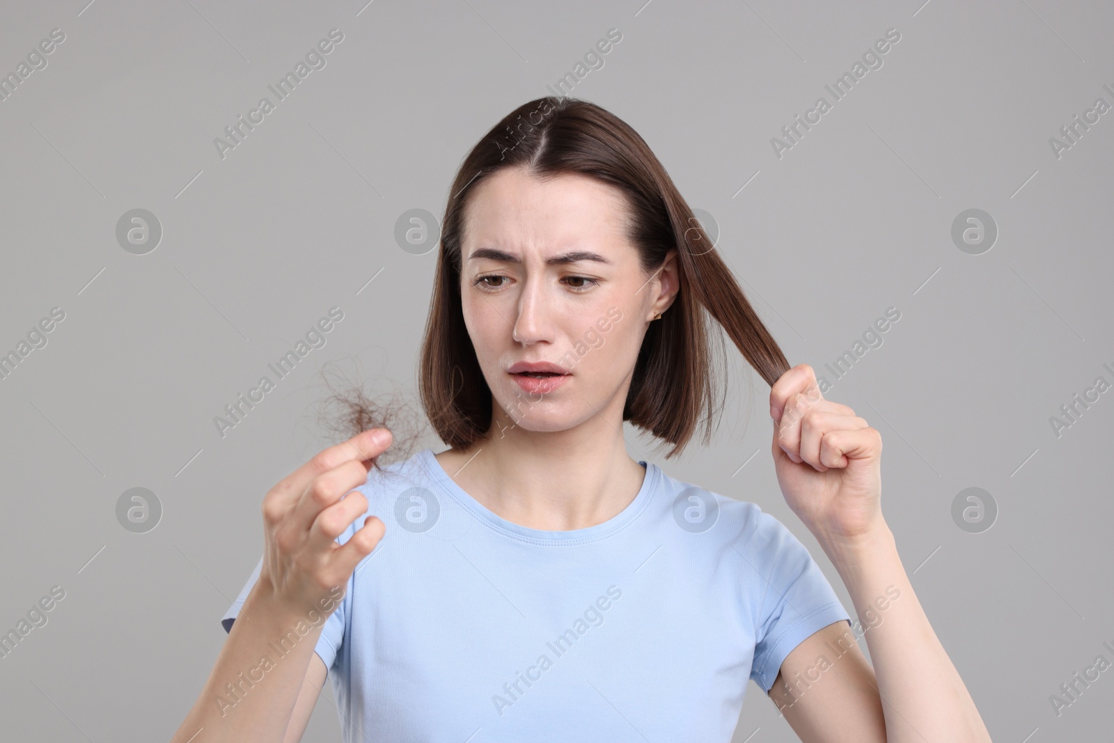 Photo of Sad woman holding clump of lost hair on grey background. Alopecia problem