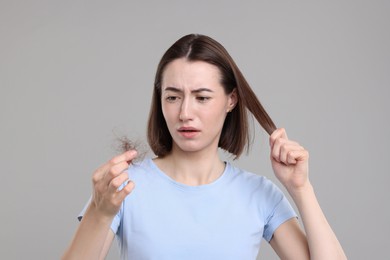 Sad woman holding clump of lost hair on grey background. Alopecia problem