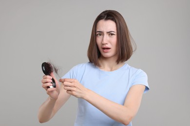 Photo of Stressed woman holding brush with lost hair on grey background. Alopecia problem